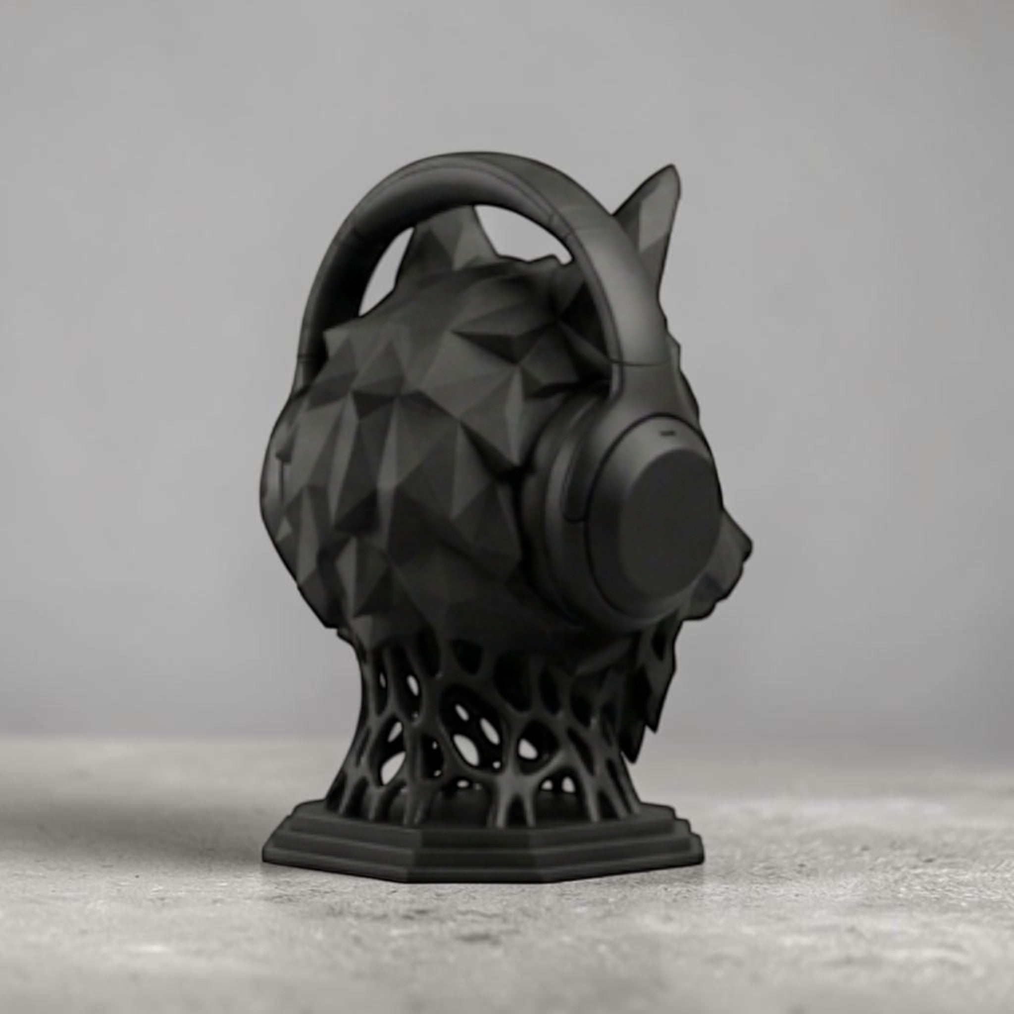Happy3dWorld matte black geometric wolf head headphone stand with a low-poly design on a grey desk surface.