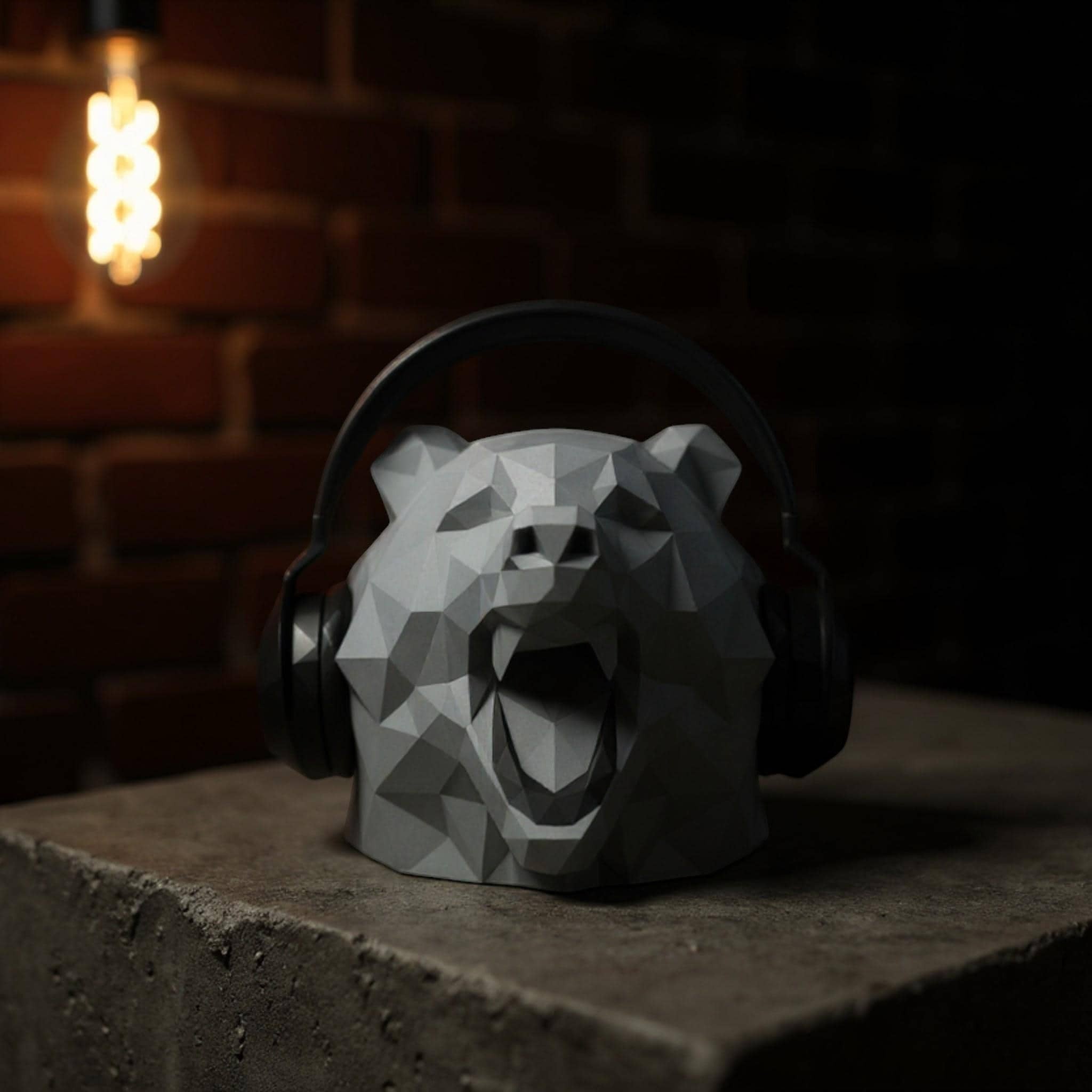 Happy3dWorld grey low polygon bear headphone stand with geometric design on a desk against a brick wall background.