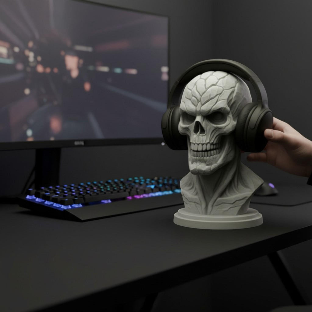 Happy3dWorld grey skull headphone stand on a gaming desk with a hand placing over-ear headphones on the bust.